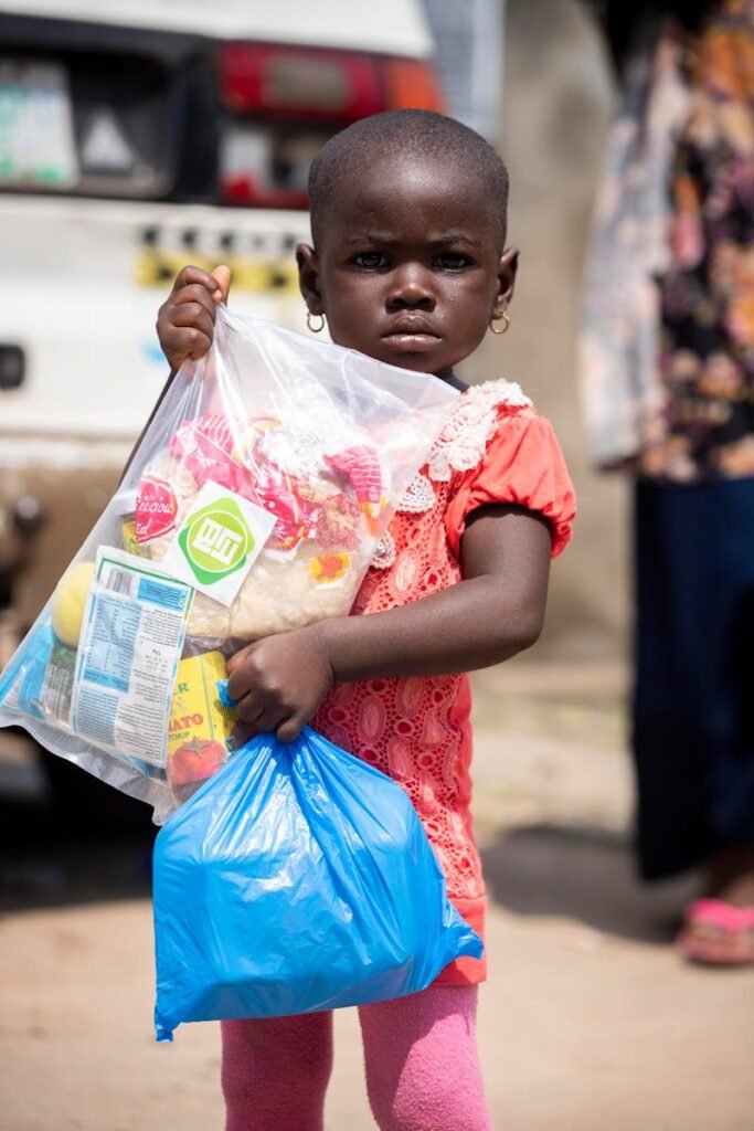 pexels-photo-8054617-8054617 A young African girl holding relief supplies in plastic bags outdoors.